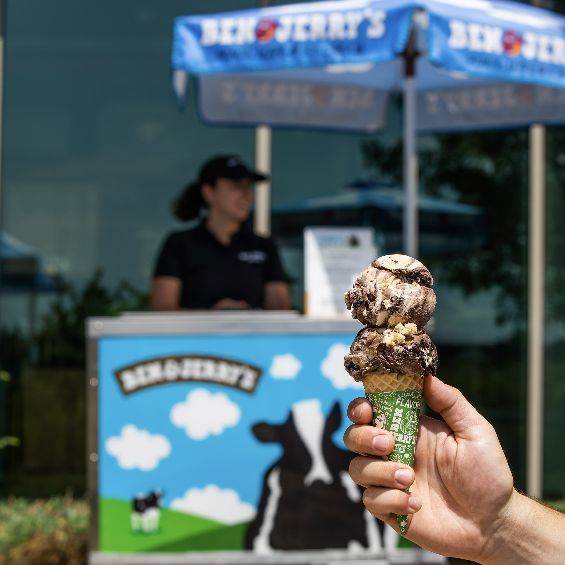 Hand holding an ice cream cone in front of a catering cart