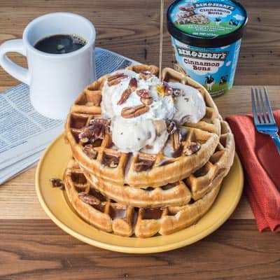 Stack of waffles with ice cream on top next to a pint of Ben & Jerry's Cinnamon Buns ice cream and a mug of coffee.