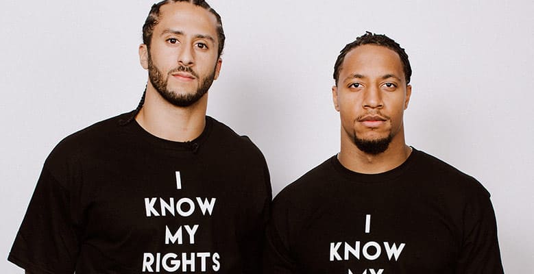 Colin Kaepernick stands next to teammate Eric Reid. Both wear shirts that say "I Know My Rights."