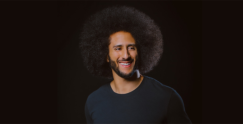 Colin Kaepernick smiling on a black background.