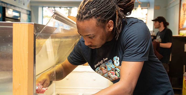 Scooper scoops ice cream into a cup at the New Avenues for Youth Scoop Shop.