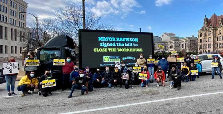 Activists and members of the Close the Workhouse Coalition in front of a sign that says MAYOR KREWSON SIGNED THE BILL THE CLOSE THE WORKHOUSE.